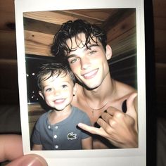 a man holding up a polaroid with a young boy pointing at the camera and smiling