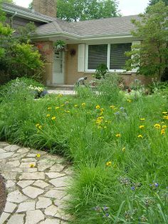 a stone path leading to a house in the middle of a yard with flowers and grass