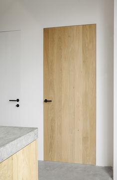 a wooden door in a white room next to a counter top and wall mounted cabinet