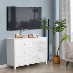 a living room with a large flat screen tv mounted on the wall above a white dresser