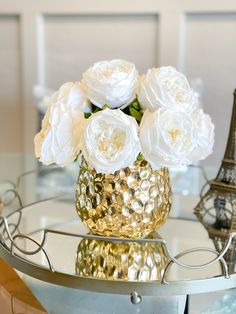 white flowers in a gold vase on a glass table with the eiffel tower in the background