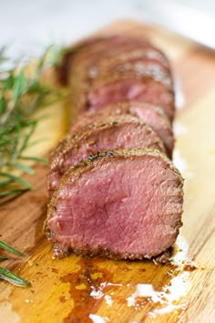 some meat is sitting on a cutting board next to rosemary sprigs and seasoning