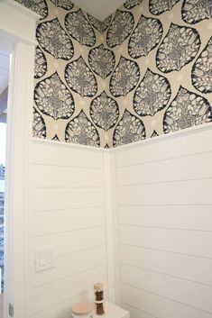 a white toilet sitting in a bathroom next to a wallpapered ceiling with black and white designs on it