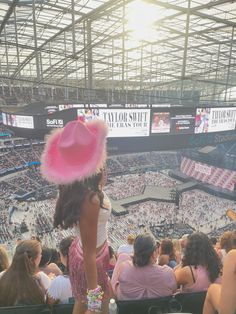 a woman wearing a pink hat standing in front of a crowd at a baseball game