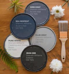 four different paint colors and brushes on a wooden table with flowers, plants and herbs