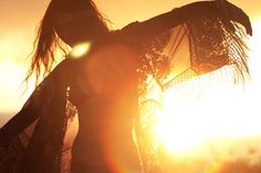 the woman is standing in front of the sun with her scarf around her neck and hands on her hips