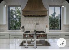 a kitchen with an oven, stove and sink in front of two windows that look out onto the trees