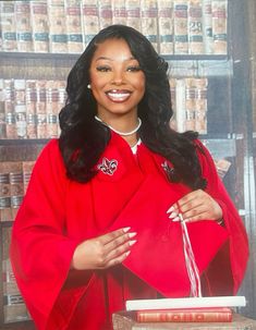 a woman in a red robe is holding a book and smiling at the camera while standing next to a bookshelf