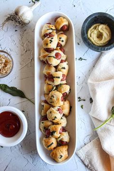 a tray filled with pigs in a blanket next to some dipping sauces and garlic