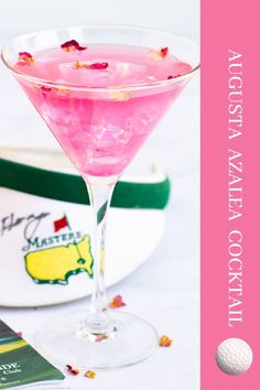 a pink drink in a martini glass with rose petals on the rim next to a golf ball