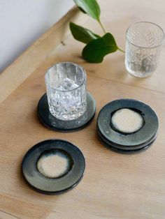 three black plates on a wooden table next to a glass with water and a plant in it