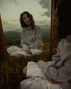 a woman sitting in front of a mirror on top of a grass covered field next to a man