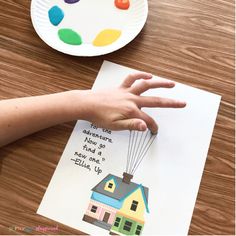 a child's hand reaching for a paper card with a house and balloons on it