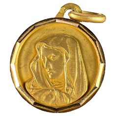 An 18 karat (18K) yellow gold charm pendant designed as a round medal with faceted frame depicting the Virgin Mary. Stamped with the eagle’s head for French manufacture and 18 karat gold, and an unknown maker’s mark. Dimensions: 2 x 1.7 x 0.1 cm (not including jump ring) Weight: 1.51 grams (Chain not included)