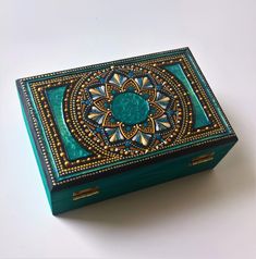 a green box with an intricate design on the lid sitting on top of a white surface