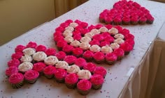 two heart shaped cupcakes on a table with pink and white frosted flowers