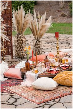 a table set up with candles, pillows and other decorative items on the ground outside