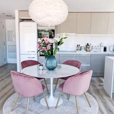 a white table with pink chairs and a blue vase on it in the middle of a kitchen