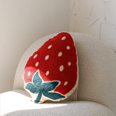 a red and white strawberry pillow sitting on top of a gray chair next to a wall