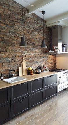 a kitchen with black cabinets and white appliances in front of a stone wall that has hanging lights above it