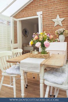 a dining room table and chairs with flowers in vases on the top, next to a brick wall