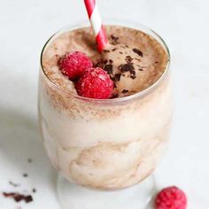 a glass filled with ice cream and raspberries on top of a white table