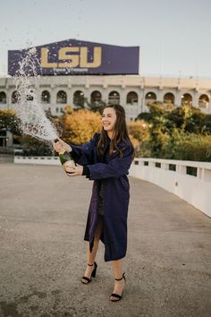 a woman is holding a bottle and spraying water on her face in front of lsu stadium