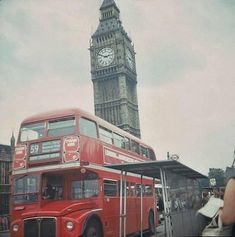 a red double decker bus parked next to a tall clock tower