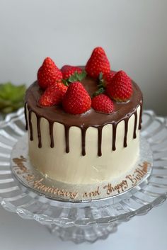 a cake with chocolate icing and strawberries on top sitting on a glass plate