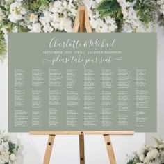 an easel with seating cards on it in front of white flowers and greenery