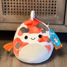 an orange and white stuffed animal with a tag on it's ear sitting on a wooden floor