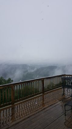 a wooden deck with two chairs on it and foggy mountains in the background