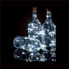 three bottles with lights in them sitting on top of a black surface and one bottle is empty