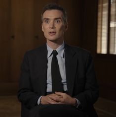 a man in a suit and tie sitting down with his hands folded on his chest