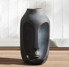 a black vase sitting on top of a hard wood floor next to a white wall