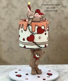 a teddy bear on top of a cake with hearts and a candle in the shape of a heart