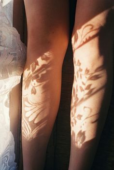 the shadow of a woman's legs and leg with flowers on them, in front of a window