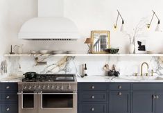 a kitchen with marble counter tops and dark blue cabinets, gold pulls on the hood