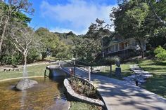 a house in the middle of a park with a bridge over water and trees around it