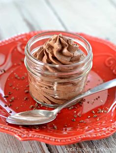 a red plate topped with a glass jar filled with chocolate frosting and sprinkles