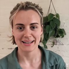 a woman with grey hair and green shirt smiles at the camera while standing in front of a white brick wall