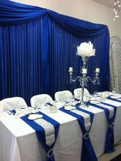 the table is set with white and blue linens, silver place settings and crystal centerpieces