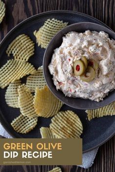 a black plate topped with chips and a bowl of dip next to some crackers