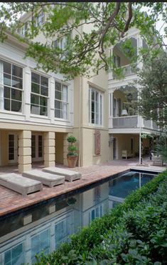 a pool in front of a large house with two lounge chairs next to the pool