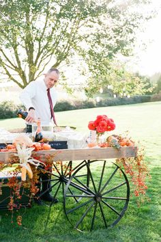 a man standing next to a wooden cart filled with food on top of a lush green field