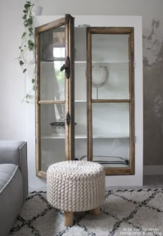 a white ottoman sitting in front of a glass doored cabinet next to a gray couch