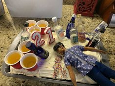 a doll laying on top of a tray filled with drinks and confetti cups