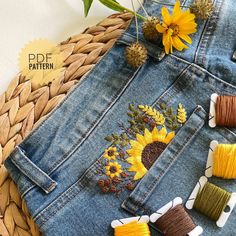 a pair of jeans with sunflowers embroidered on them and some spools of thread