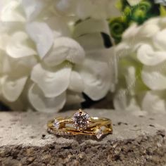 two wedding rings sitting on top of a rock with white flowers in the back ground