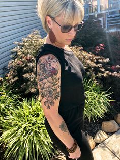 a woman with a tattoo on her arm standing in front of some plants and bushes